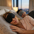 Two people lying in bed wearing eye masks in a bedroom setting.
